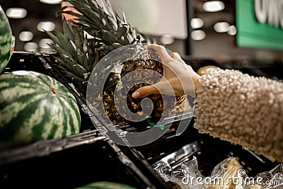 Woman makes purchases in department of vegetables, fruits in store. Hand holds pineapple selection of products. Diet. Vitamins and Stock Photo