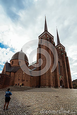 A woman makes a video of the exterior of The Cathedral of Saint Luke in Roskilde, Denmark, with a gimbal standcam for smartphone Editorial Stock Photo