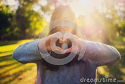 Woman making heart hand sign in the park before sunset Stock Photo