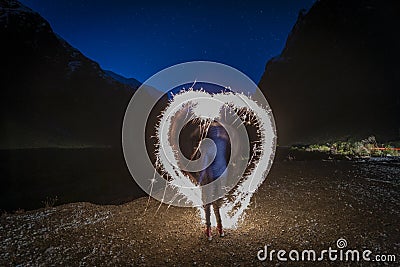 Woman making a heart shape with a sparkler at night with towering cliffs in the background o Stock Photo