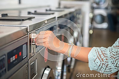 Woman making payment putting quarter to washing laundromat machine in public laundry Stock Photo