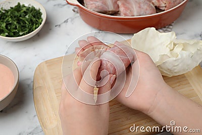 Woman making stuffed cabbage roll at white table, closeup Stock Photo