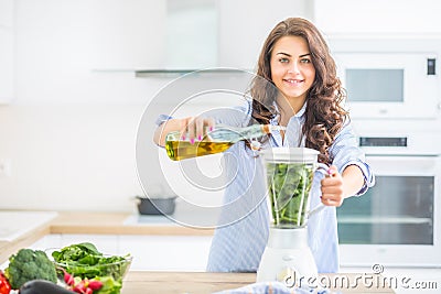 Woman making vegetable soup or smoothies with blender in her kitchen. Young happy woman preparing healthy food or drink with olive Stock Photo