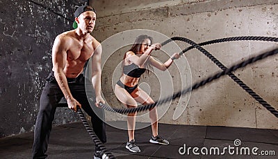 Woman and man couple training together doing battling rope workout Stock Photo