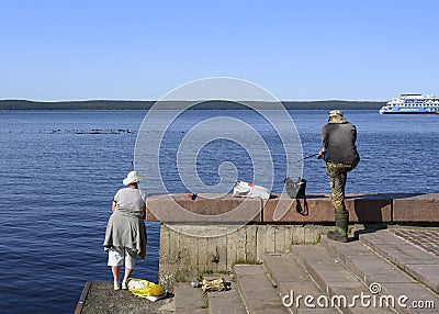 A woman and a man fishing on the embankment of Lake Onega near the pier with tourist ships Editorial Stock Photo