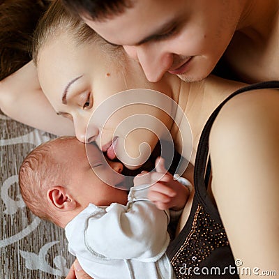 Woman and man lie on bed together with newborns. Mom, dad and baby. Boy clung to his mother. Portrait of young smiling family with Stock Photo