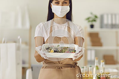 Woman in a mask gives the client a ready fresh healthy lunch in a plastic container. Stock Photo