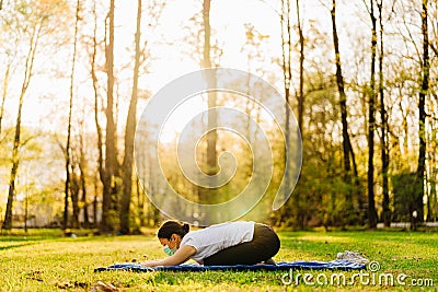 Woman with mask meditating/practicing yoga in nature alone.Social distancing and active healthy lifestyle. Mindfulness meditation. Stock Photo