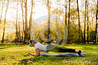 Woman with mask meditating/practicing yoga in nature alone.Social distancing and active healthy lifestyle. Mindfulness meditation. Stock Photo