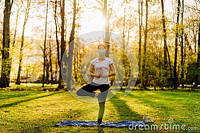 Woman with mask meditating/practicing yoga in nature alone.Social distancing and active healthy lifestyle. Mindfulness meditation. Stock Photo