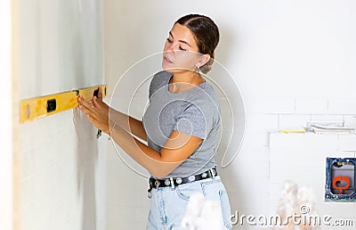 Woman measures deviations from predetermined vertical wall using building level Stock Photo