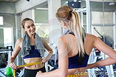 Woman measuring waist in gym. Slim woman measuring her thin waist with a tape measure. smiling people with measure tape in the Stock Photo