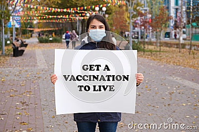 A woman in a medical mask holds a poster that says Get a vaccination to live Stock Photo