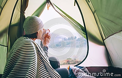 Woman meets cold morning sitting in touristic tent with cup of hot tea. Active vacation concept image. Stock Photo