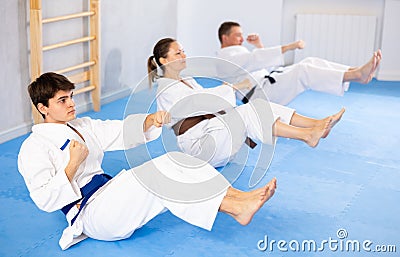 Woman and men in kimono train abdominal muscles and do punches at same time during karate or judo training Stock Photo