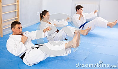 Woman and men in kimono train abdominal muscles and do punches at same time during karate or judo training Stock Photo