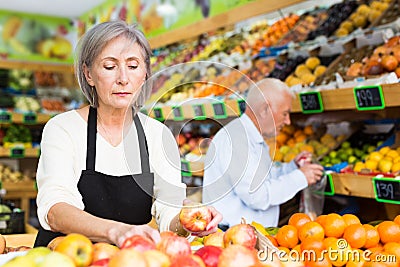 Woman merchandiser in apron putting goods on shelf in supermarket Stock Photo