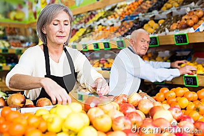 Woman merchandiser in apron putting goods on shelf in supermarket Stock Photo