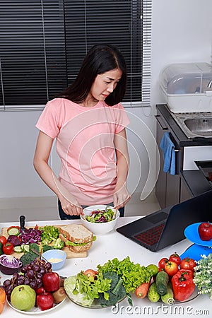 Woman mixing salad while cooking with laptop in kitchen Stock Photo