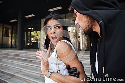 Woman with mobile phone shouting and attacked by criminal man Stock Photo