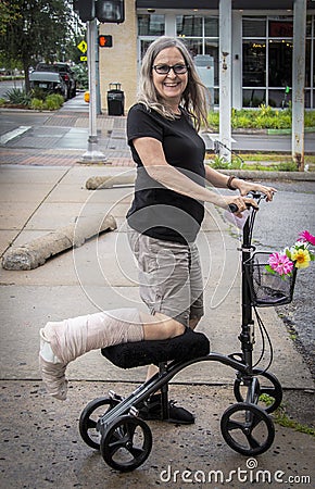 Woman on mobility scooter on street with leg wrapped smiling at camera Stock Photo