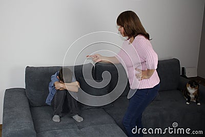 Woman, mother, scolding her son, showing with an accusatory hand, kid sitting with her hands closed on the couch, concept of Stock Photo