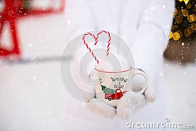 Woman with mug with snow, candy cane and inscription Merry and Bright in her hands outdoor in warm clothes in winter festive Stock Photo