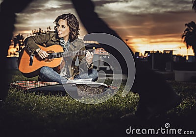 woman musician plays her guitar in a park while people pass by indifferently in front of her Stock Photo