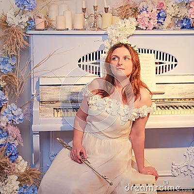 Woman musician sits with a flute on the background of a piano decorated with flowers Stock Photo