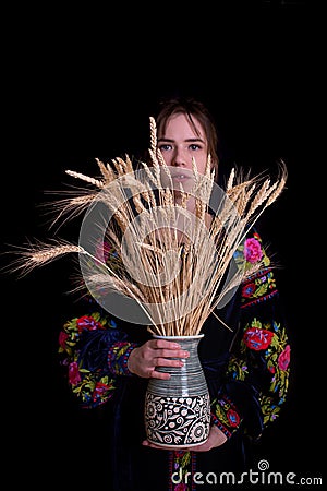 Woman in national dress holding a bouquet of dry wheat in a vase. On black bakground. Face covered with wheat Stock Photo