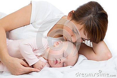 Woman and newborn boy relax in a white bedroom. Young mother kissing her newborn child. Mom nursing baby. Stock Photo
