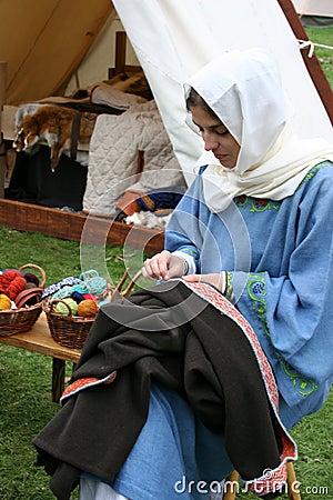 A woman in a Norman costume mending a garment at The reenactment of The Battle of Hastings Editorial Stock Photo