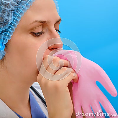 Woman nurse blows up a pink medical glove, close-up on a blue background. Doctor puff a protective glove with air, concept Stock Photo