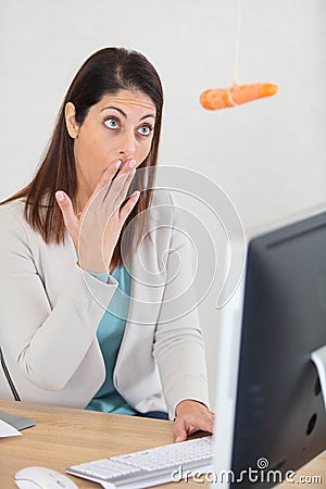 woman at office desk looks in surprise at dangling carrot Stock Photo