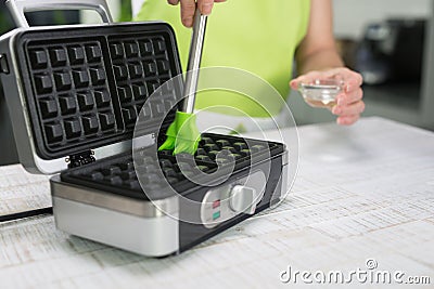 Woman is oiling the waffle iron in her modern kitchen Stock Photo