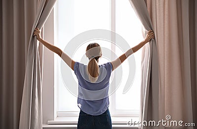 Woman opening curtains and looking out of window Stock Photo