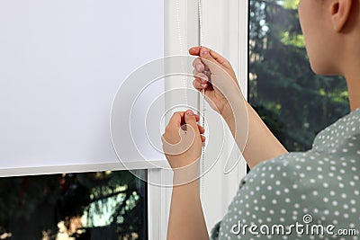 Woman opening white roller blind on window, closeup Stock Photo