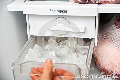 A woman opens an ice maker tray in the freezer to take ice cubes to cool drinks Stock Photo