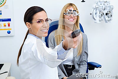 Woman optometrist with trial frame checking patient`s vision at eye clinic. Selective focus on doctor. Stock Photo