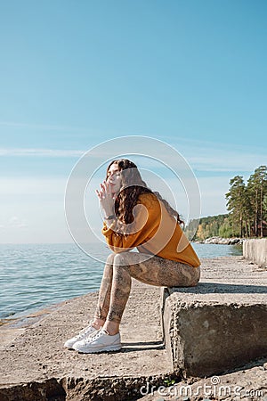 Woman in orange sweater sitting on a stone stairs on a beach with her eyes closed Stock Photo