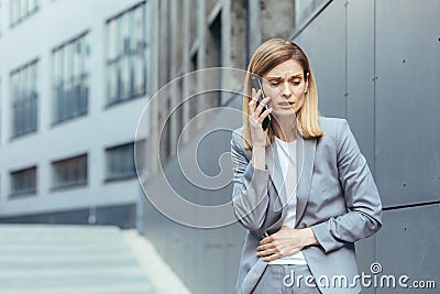 Woman outside the office has severe abdominal pain, tries to call the doctor uses the phone Stock Photo