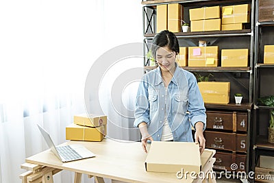 Woman packing box on table checking goods package delivery shipping to customer. Asian woman startup small business at home office Stock Photo