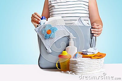 Woman packing diaper bag on blue background. Stock Photo