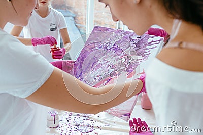 Woman painter holding hair dryer while female beginnres studying creating fluid acrylic abstract painting in art therapy Stock Photo