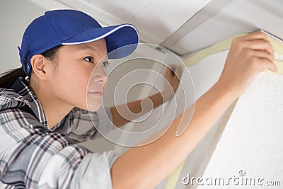 woman painter worker protecting ceiling moulding with masking tape Stock Photo