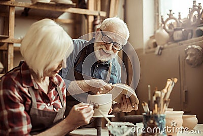 Woman painting clay pot with senior potter Stock Photo