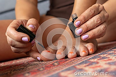 Woman painting her toenails with orange nail polish Stock Photo