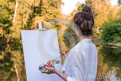 woman paints picture landscape, girl artist, view back, summer park lake pond river, white shirt , creating creativity Stock Photo