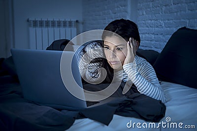 Woman in pajamas on bed at home bedroom working bored and tired with laptop computer Stock Photo