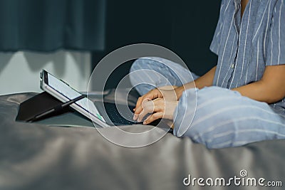 Woman in pajamas sitting on bed in bedroom working with laptop. Stock Photo